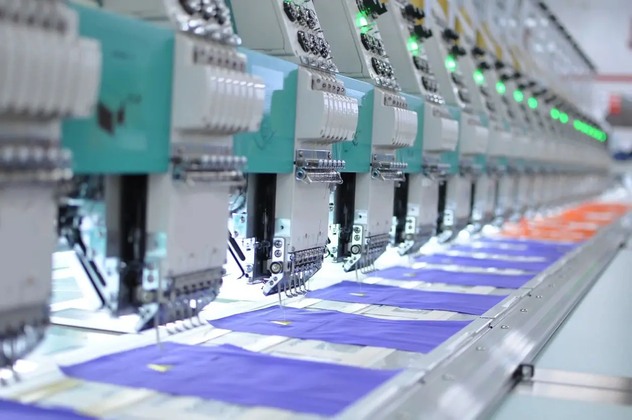 A row of machines in a factory with blue fabric on the sewing machine.